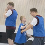 Fyra deltagre med blå västar på sig. Två tittar på varandra och ler, är påväg att kramsa.